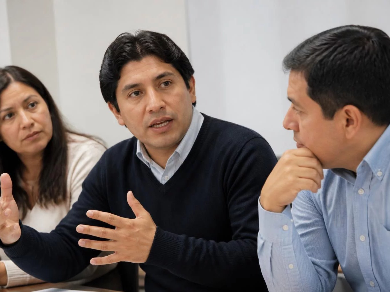 Reunión de tres personas en una sala clara, con alguien exponiendo
